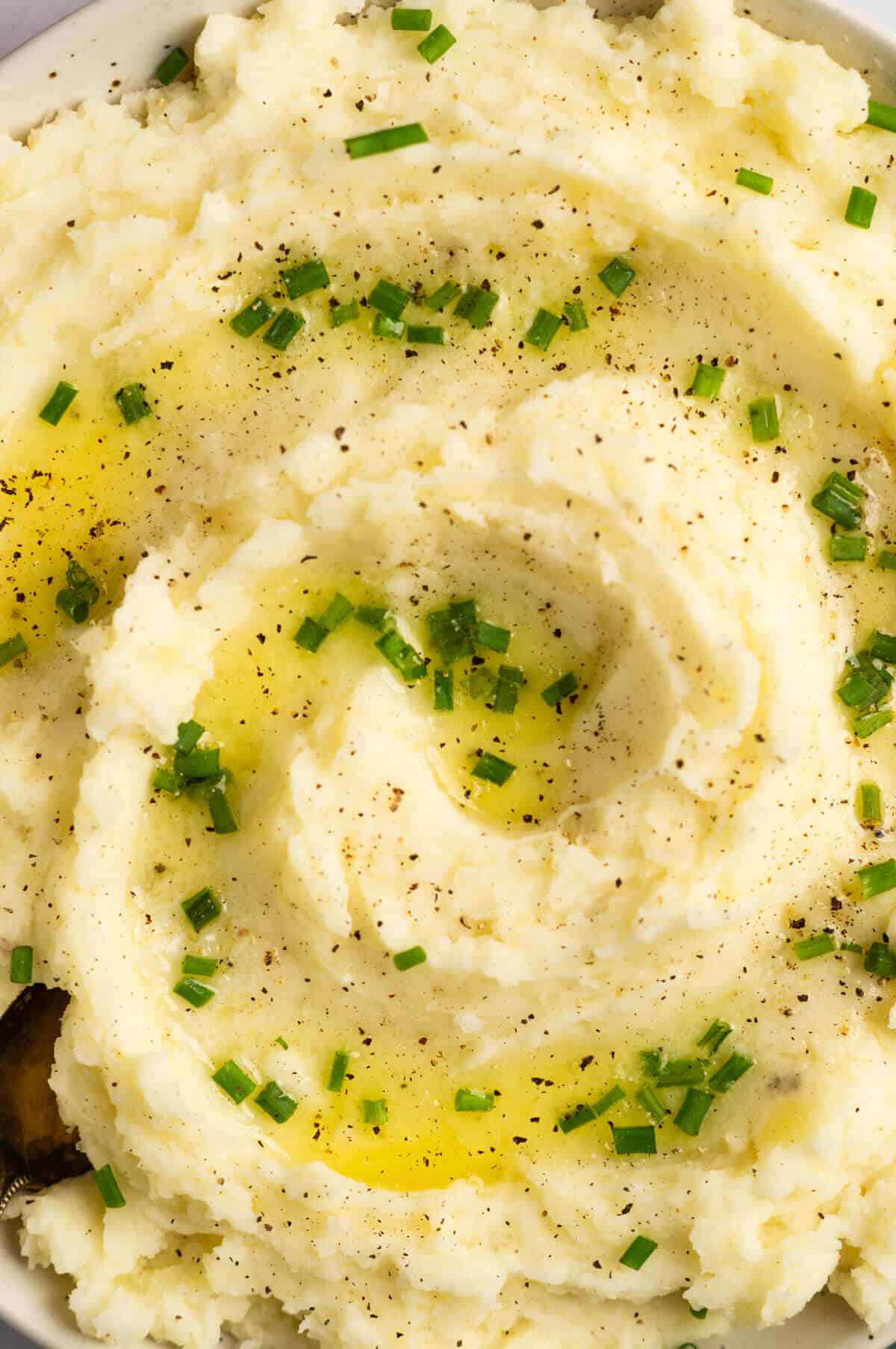 A close up shot of Greek yogurt mashed potatoes with chives, black pepper, and melted butter on top.