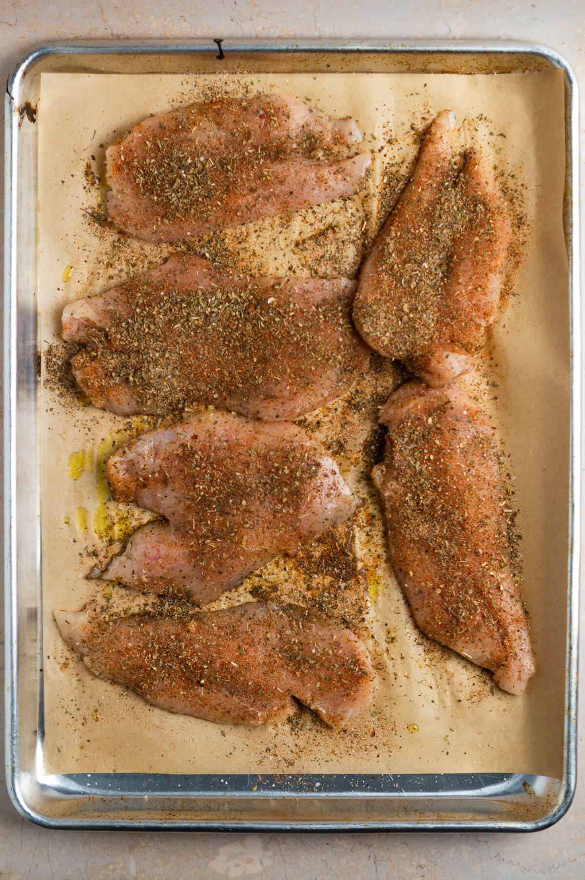 A parchment-lined baking sheet with 6 pieces of chicken breast coated in the herb mixture.