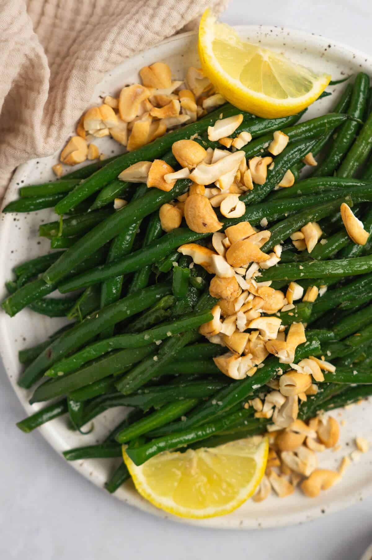 A close up shot of a plate of honey roasted green beans with roasted cashews.
