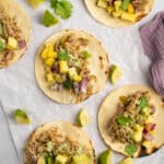 Overhead shot of slow cooker salsa verde pork on tacos with lime, avocado, cilantro, and pineapple.