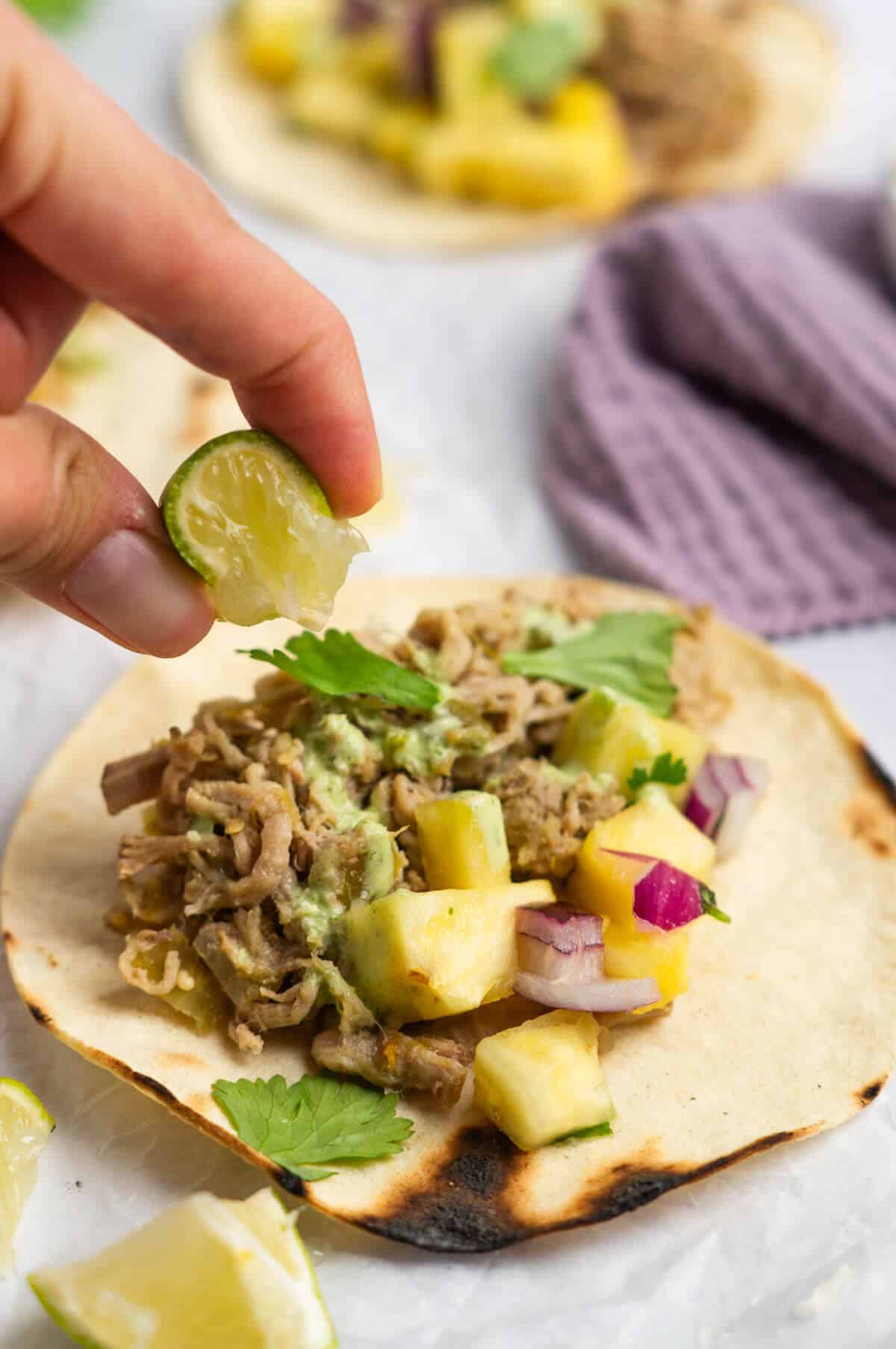 A taco with salsa verde pork with a lime being squeezed over the top.