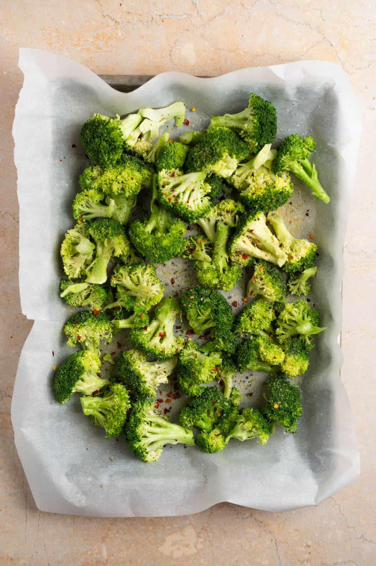 A baking dish with broccoli seasoned with salt, pepper, and red pepper flake.