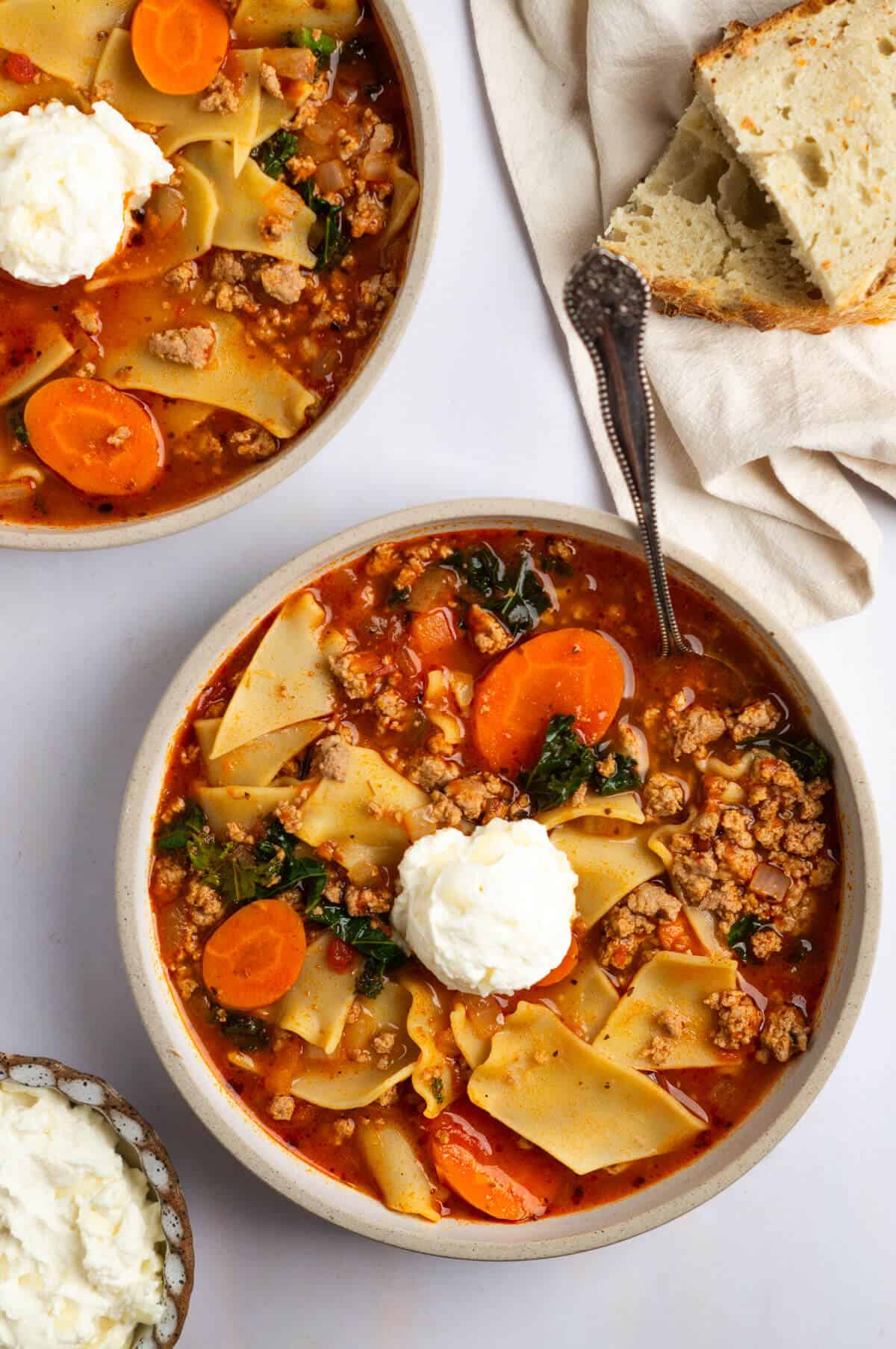 An overhead shot of two bowls of turkey lasagna soup with bread on the side.