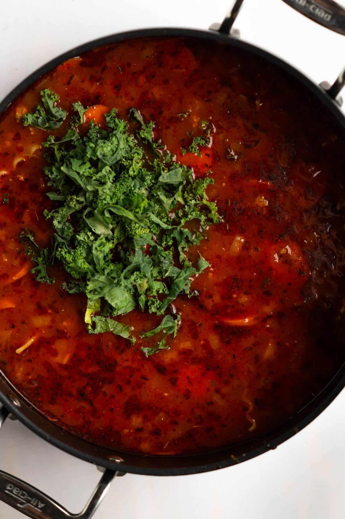 A large soup pot with turkey lasagna soup and chopped kale added into the soup.