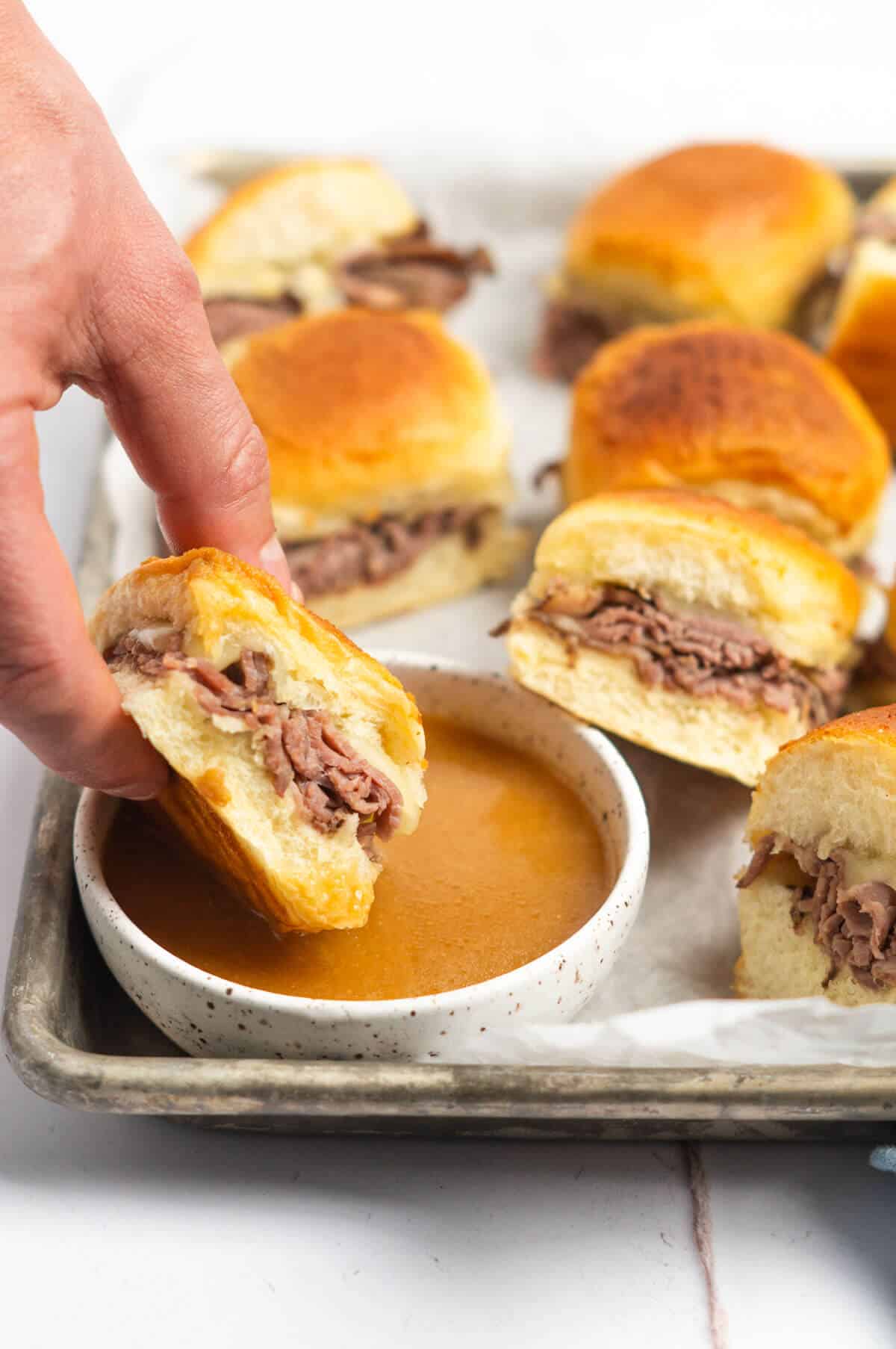 A roast beef slider being dipped into the au jus dipping sauce.