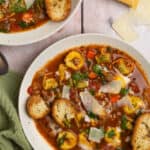 A bowl of tortellini soup with toasted slices of baguette.