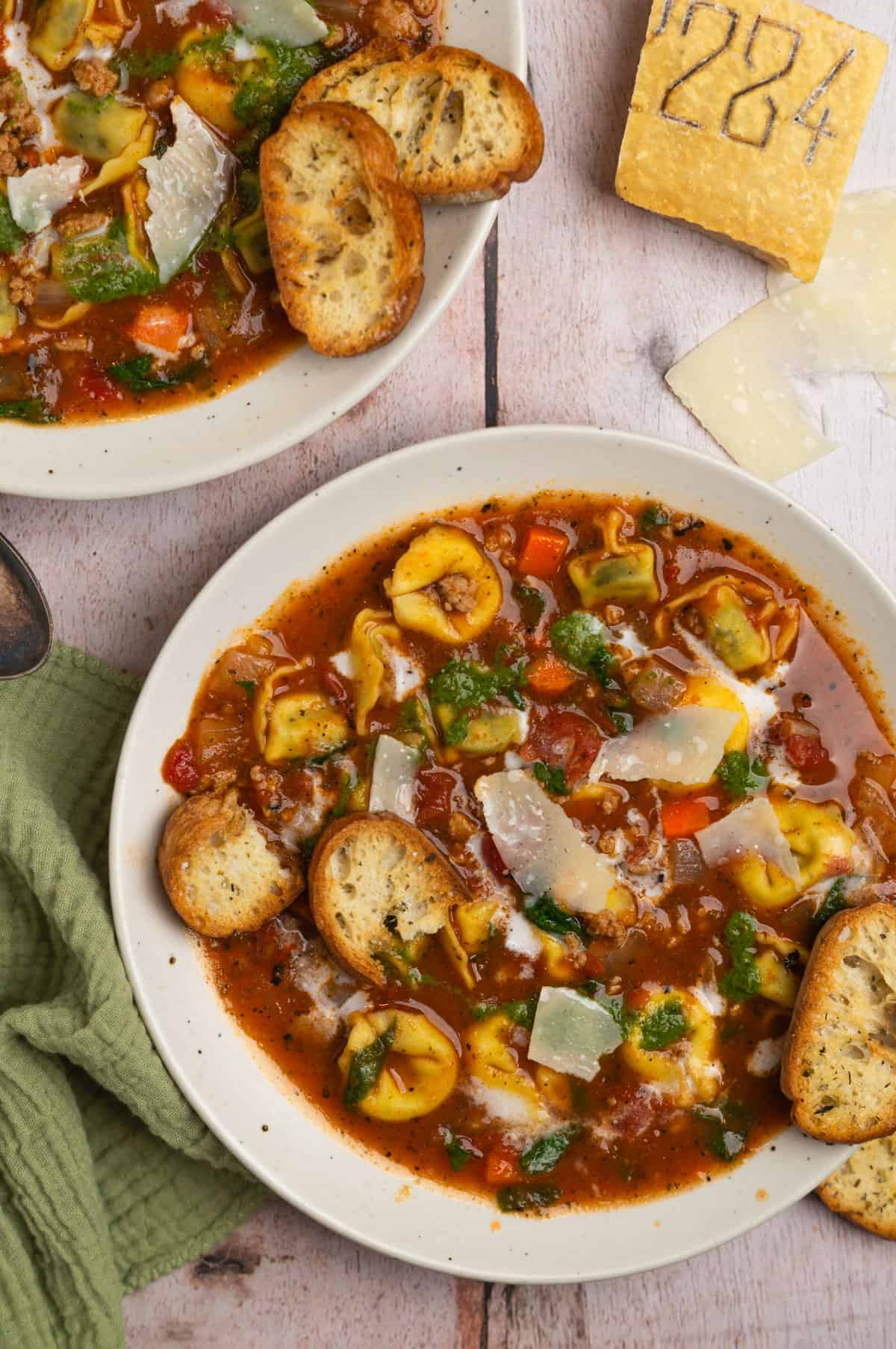 A bowl of tortellini soup with toasted slices of baguette.