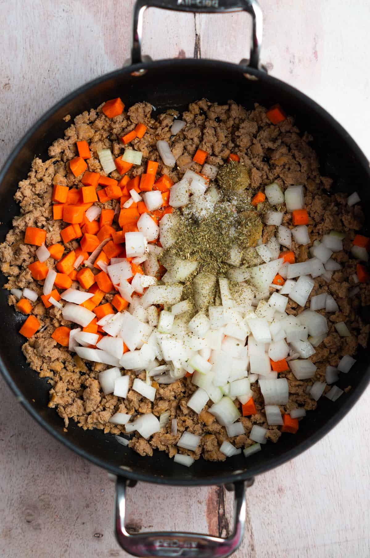 A large pot with cooked sausage, chopped veggies, and spices.