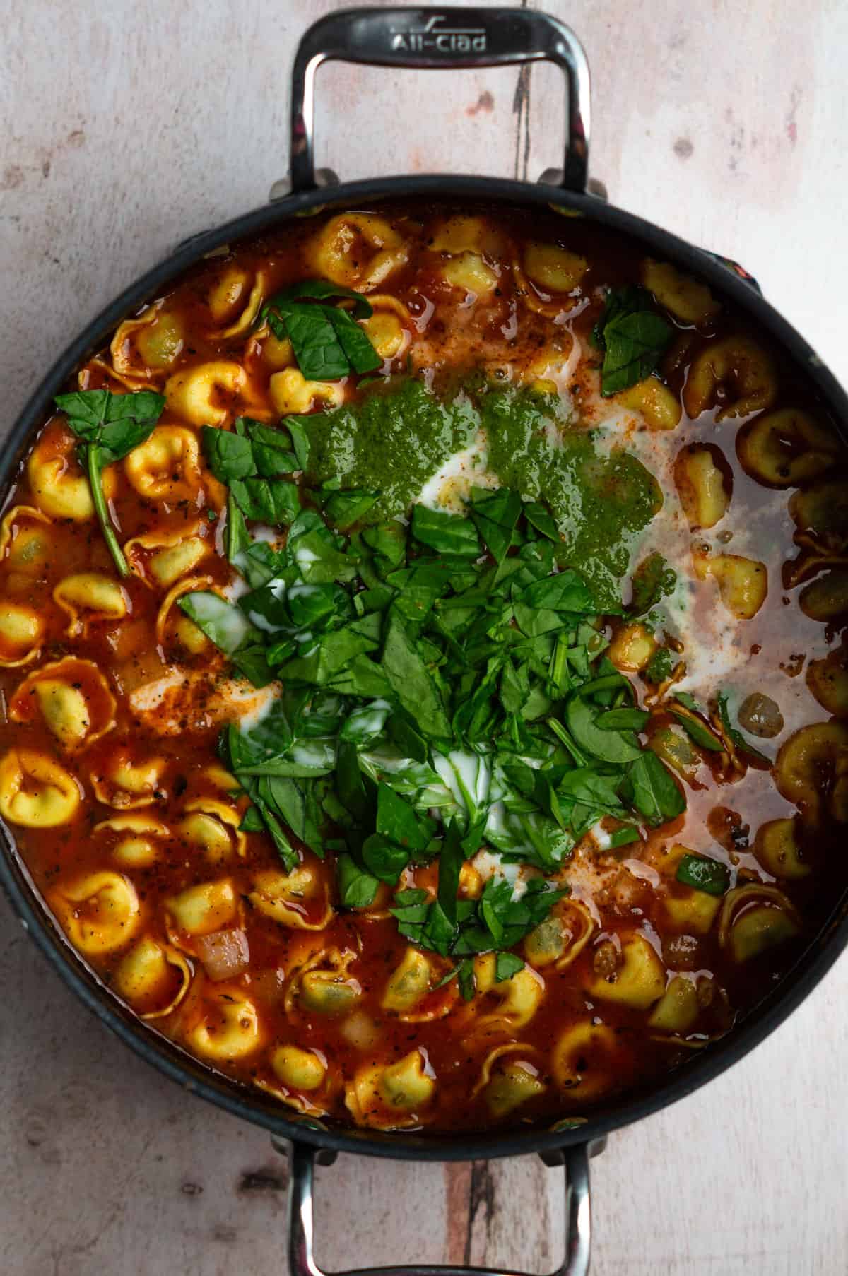 A large soup pot with the tortellini and chopped spinach added to the soup.