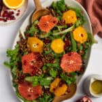 Overhead shot of pomegranate winter salad with tongs and dressing.