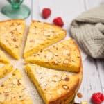 Almond cake cut into slices and garnished with powdered sugar and raspberries.