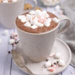 A mug of hot chocolate topped with mini marshmallows, crushed candy cane, and mini chocolate chips.