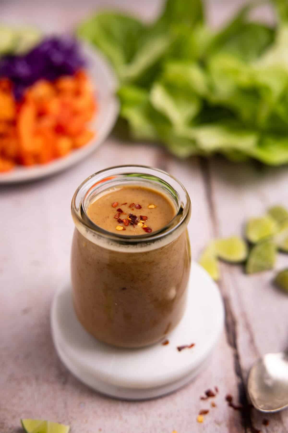 Jar of peanut sauce with vegetables in background.