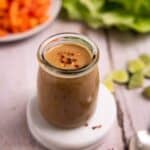 Jar of peanut sauce with vegetables in background.