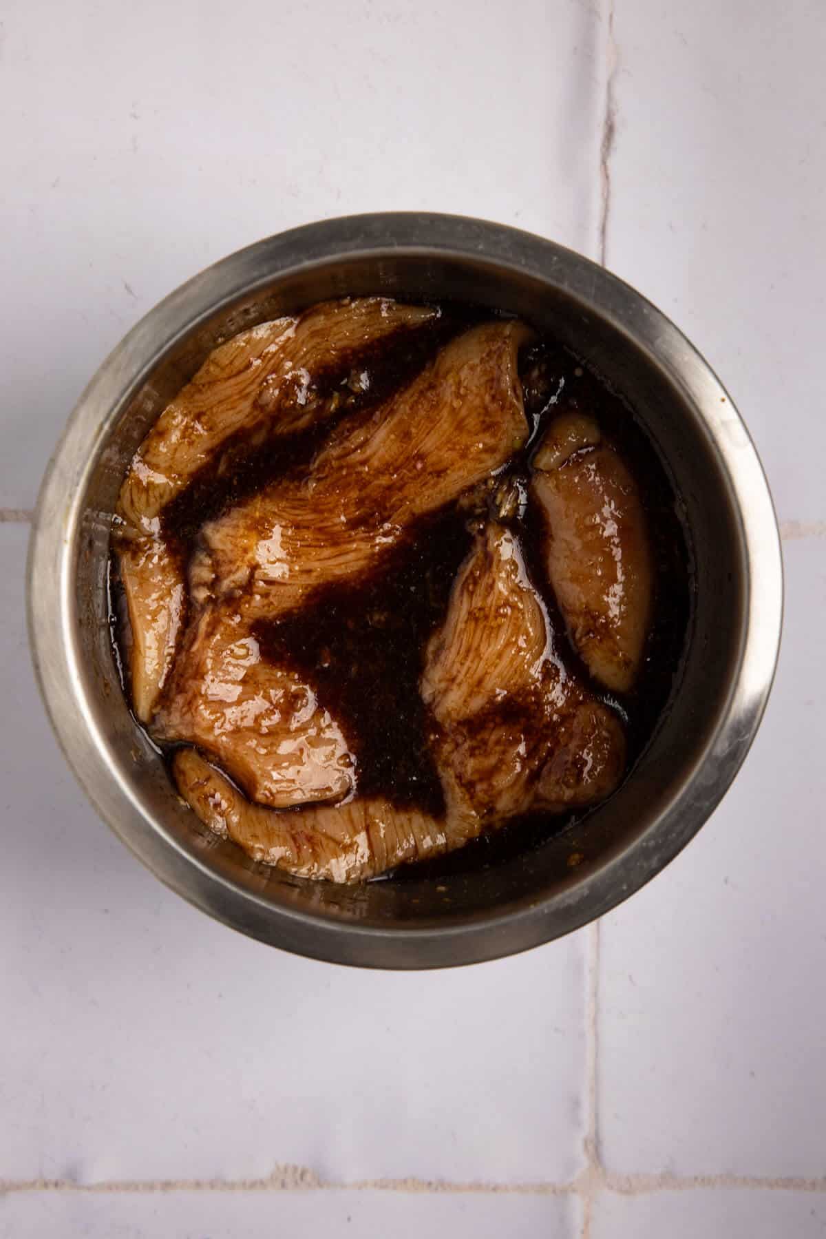 A large bowl with marinating chicken.