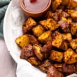 A bowl lined with parchment paper, filled with air fryer red potatoes and a small bowl of ketchup.