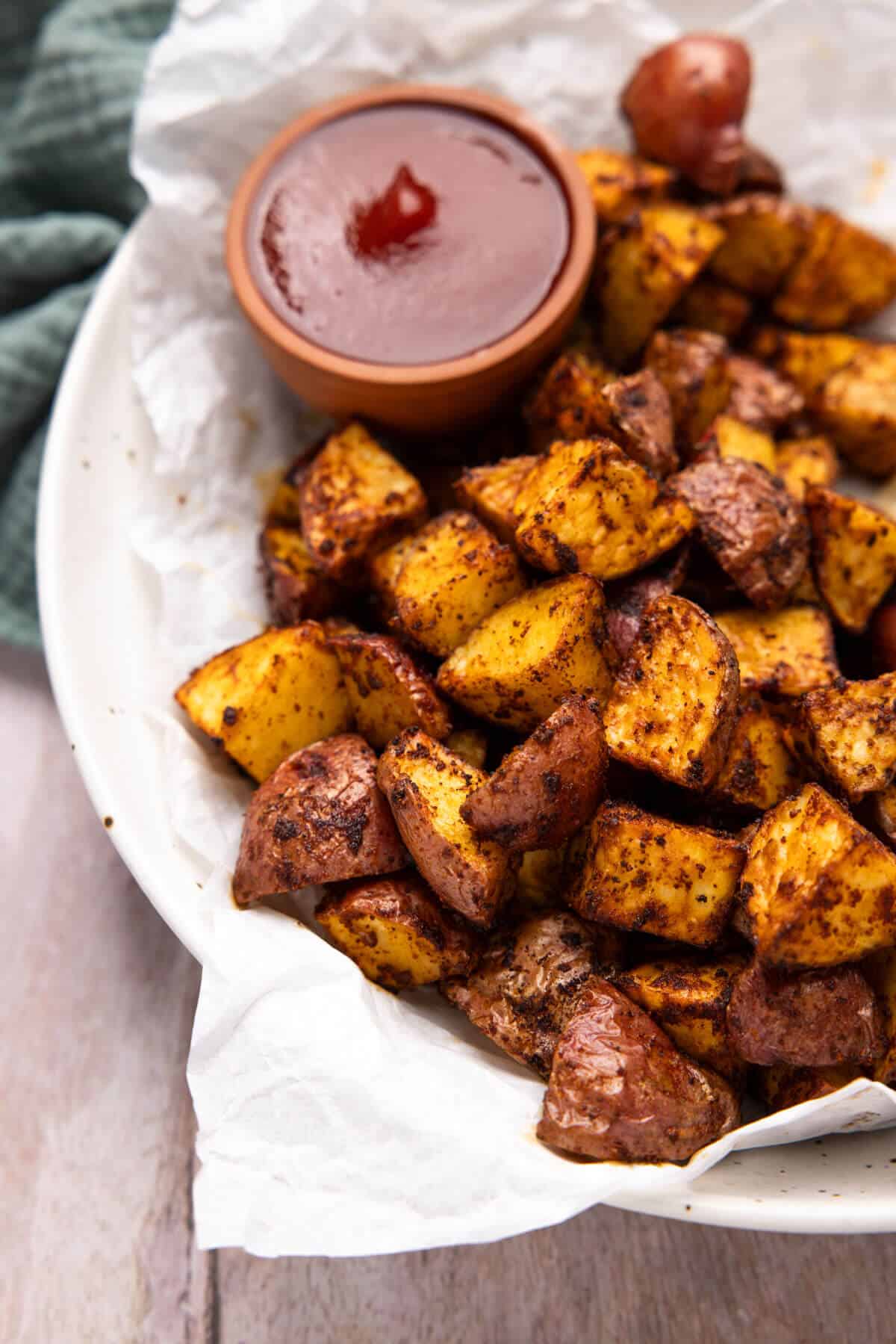 A bowl lined with parchment paper, filled with air fryer red potatoes and a small bowl of ketchup.