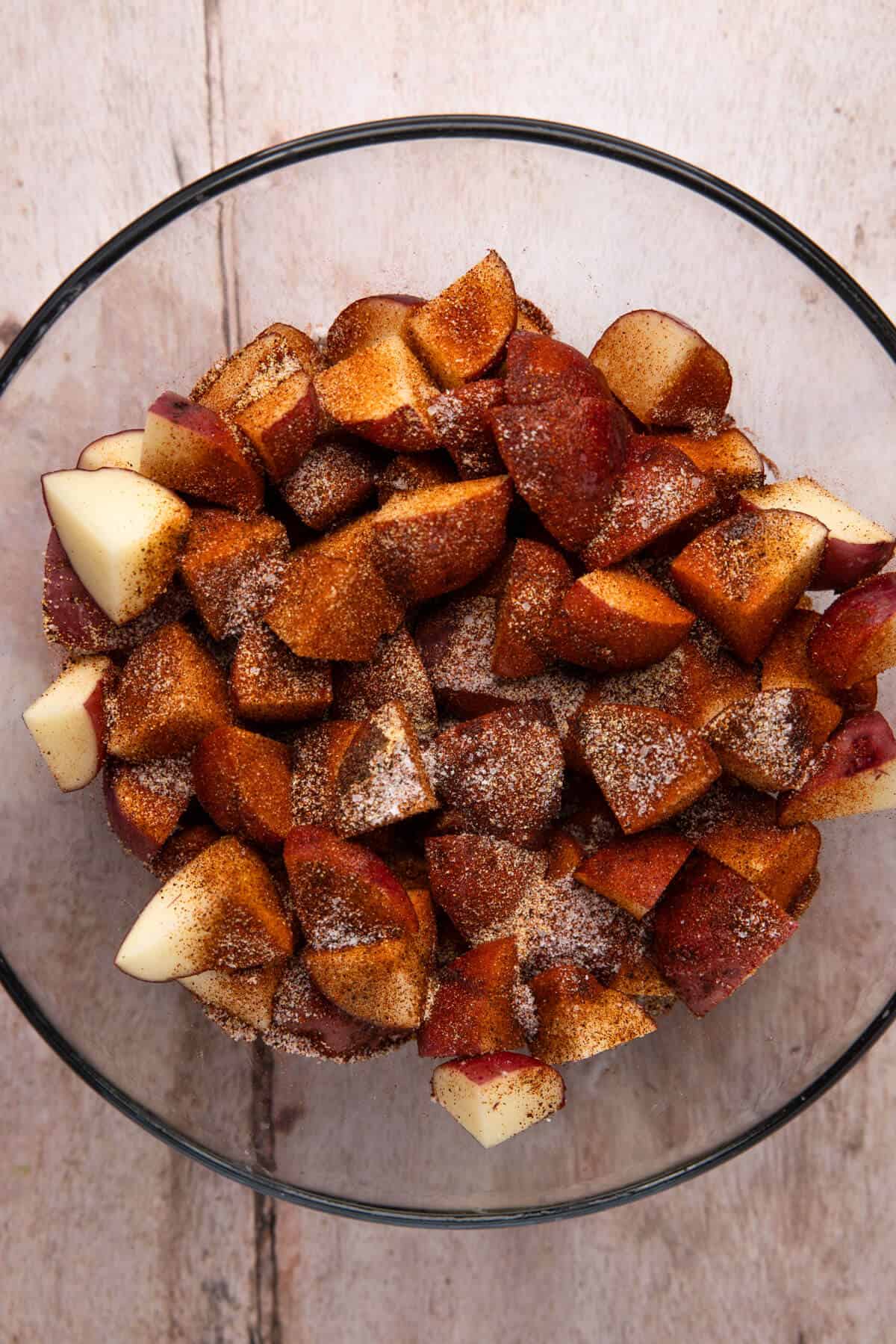 A large mixing bowl with cut red potatoes, olive oil, and spices, unmixed.