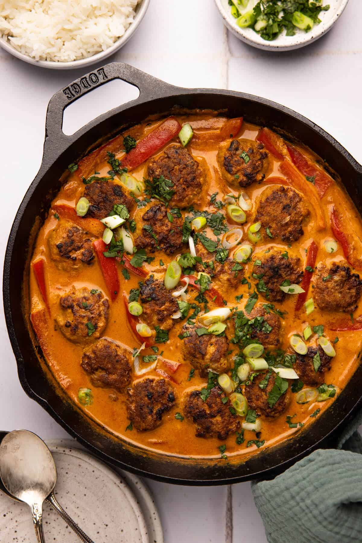 Large pan with curry meatballs and rice, green onion, and cilantro.