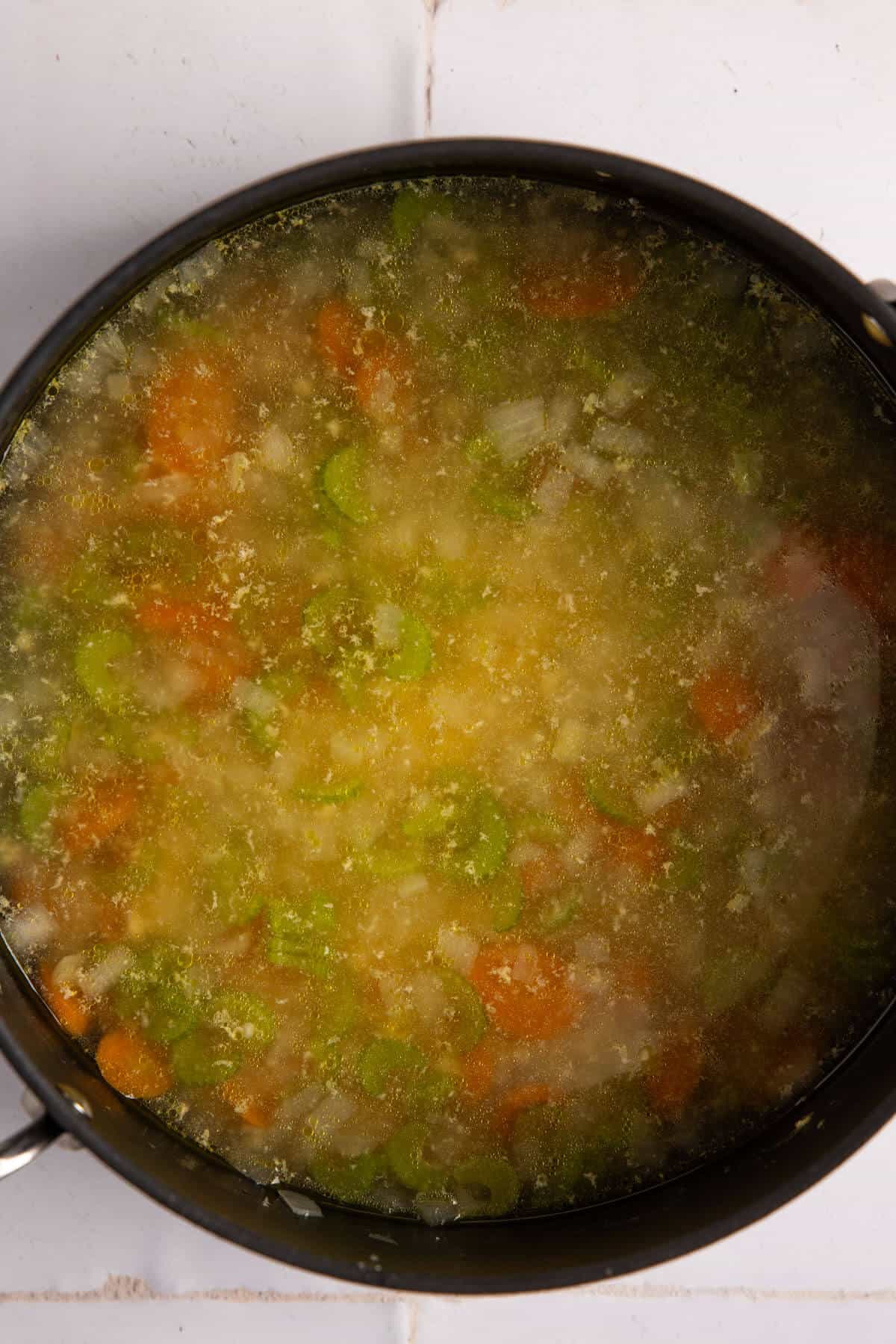 An overhead shot of a large soup pot with orzo pasta stirred in.