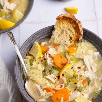 A bowl of Greek lemon orzo soup garnished with fresh lemon and a crusty baguette slice.