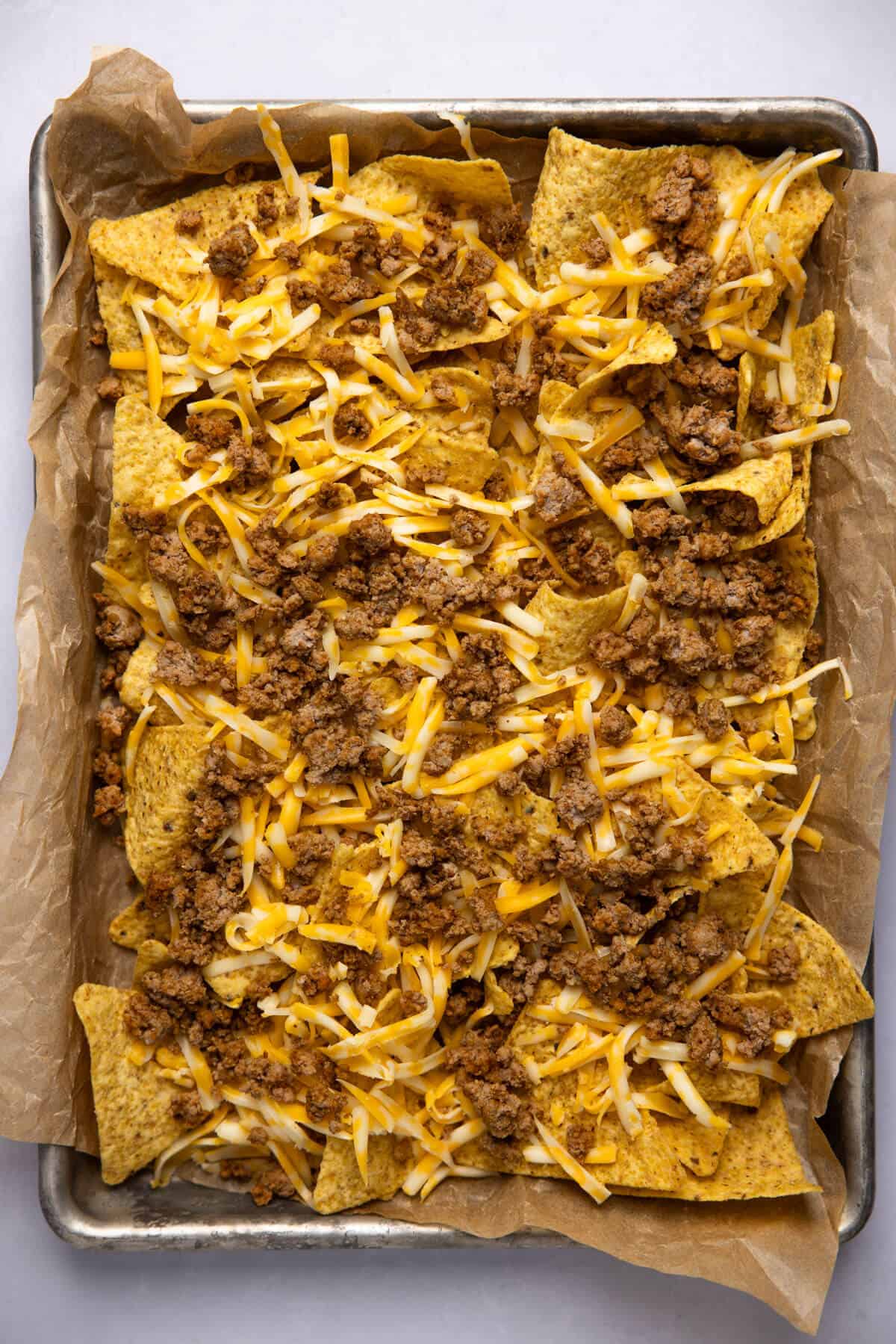 A parchment lined baking sheet with cooked ground turkey and shredded cheese.