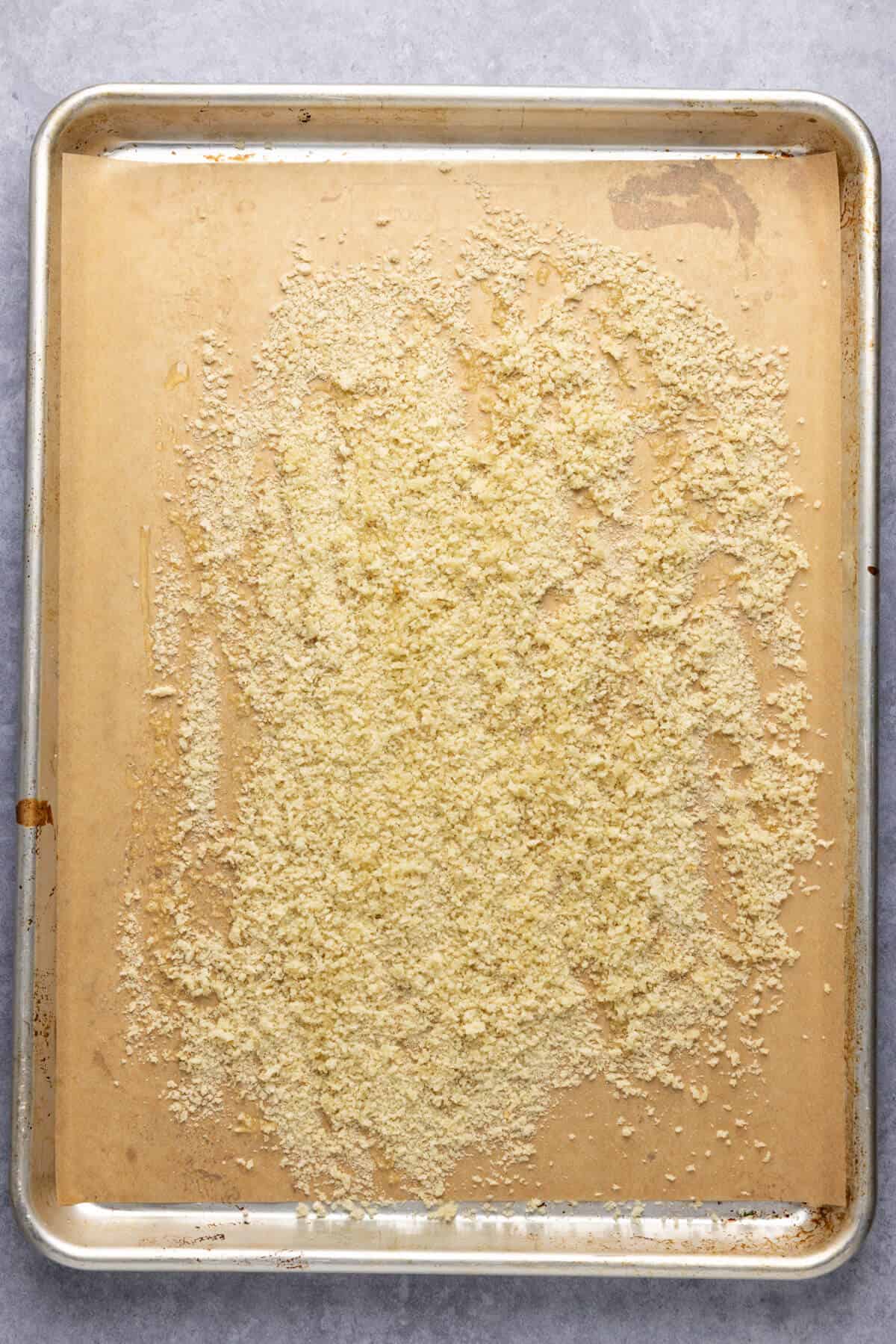 A parchment-lined baking sheet with bread crumbs on top.