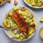 An overhead shot of a plate with blackened salmon caesar salad and homemade croutons, garnished with lemon.