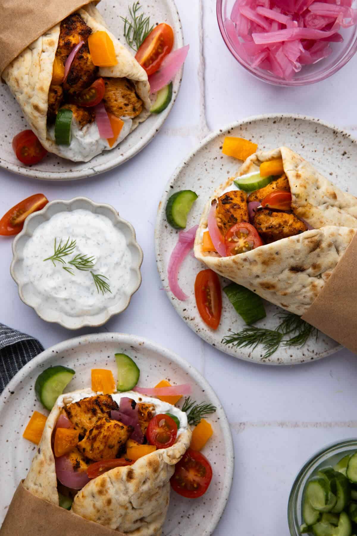 Three plates with assembled Greek chicken wraps.