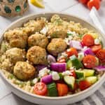 A close up shot of Greek chicken meatballs in a bowl with quinoa and Greek salad.
