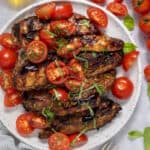 A serving plate with grilled balsamic chicken garnished with grape tomatoes and fresh basil.