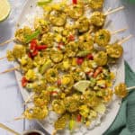 A large platter of oven baked shrimp skewers served over a bed of rice with mango salsa.