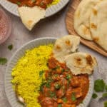An overhead shot of plates of crockpot chicken tikka with yellow rice and naan.