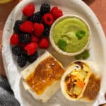 A serving platter with a halved breakfast burrito, avocado salsa, and fresh berries.