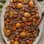 Overhead shot of a serving platter of crockpot chuck roast with carrots, potatoes, onions, and roast.