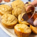 A side shot of a serving platter of pancake bites with maple syrup being drizzled on top.