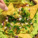 A hand dipping a tortilla chip into a bowl of guacamole.