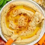Overhead shot of homemade hummus with pita bread and a carrot stick being dipped into it.