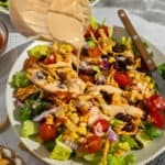 Plated BBQ ranch chicken salad with BBQ ranch dressing being poured over the top.