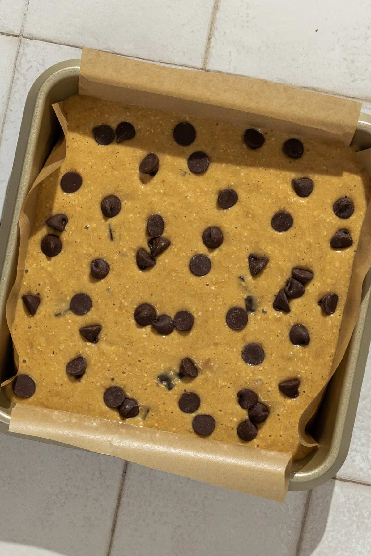 Batter for banana peanut butter bars poured into a parchment lined square baking dish and chocolate chips sprinkled on top.