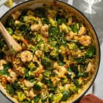 A large skillet with the cooked shrimp and orzo meal.