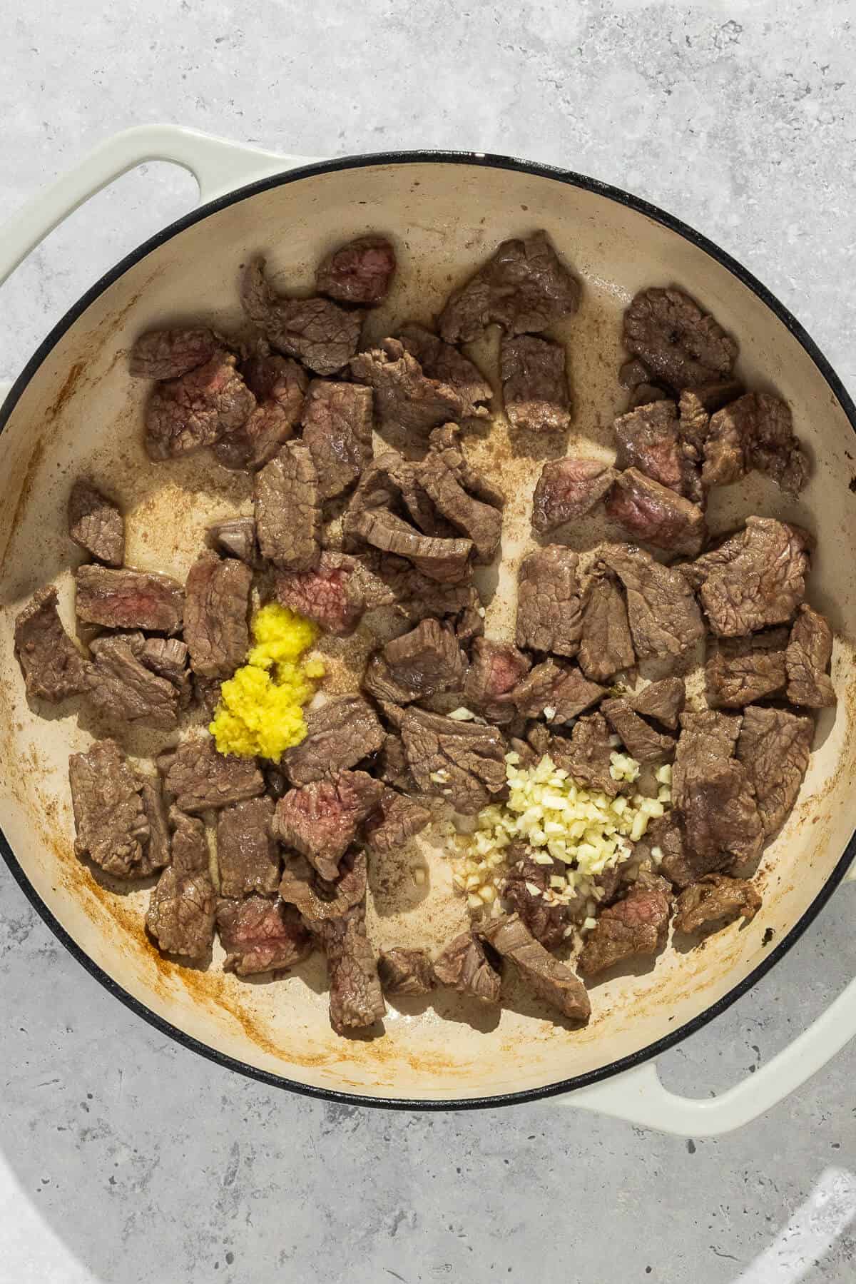 A large pan of cooked pieces of beef with minced garlic and ginger.
