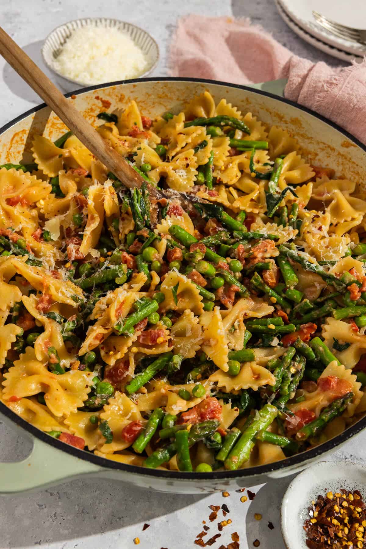 Completed bowtie pasta with spring vegetables in a large pot with a wooden serving spoon.