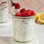 Glass mason jar of lemon chia pudding topped with raspberries being scooped out with a spoon.