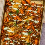 Cooked sheet pan chicken thighs and vegetables with the herbed yogurt sauce drizzled over the top.