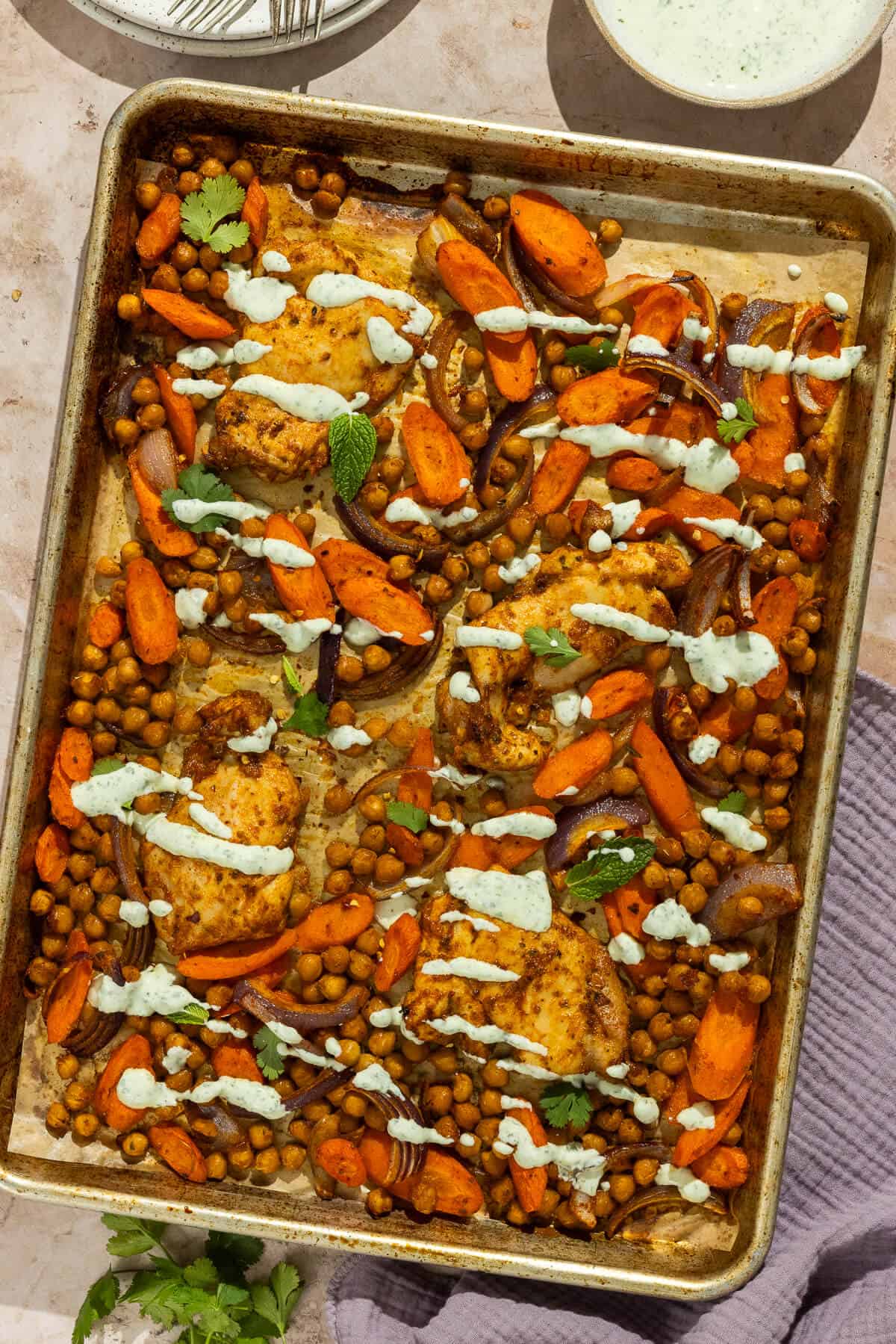 Cooked sheet pan chicken thighs and vegetables with the herbed yogurt sauce drizzled over the top.