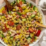 A large serving bowl of grinder pasta salad with two wooden serving spoons.