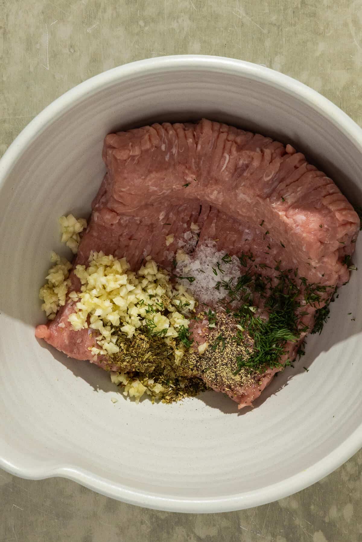 A mixing bowl with ground chicken and spices prior to mixing.