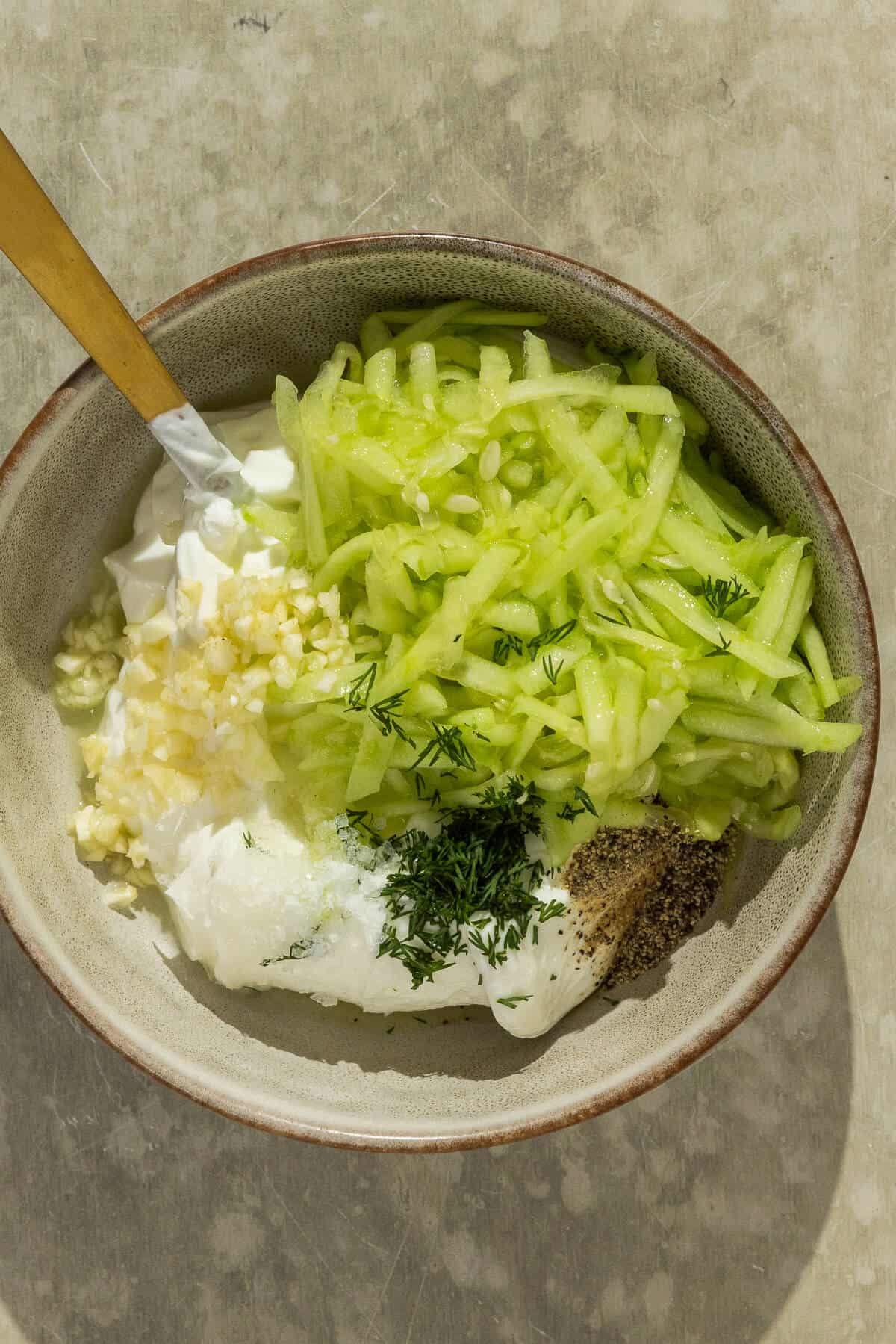 A mixing bowl with homemade tzatziki sauce prior to mixing.