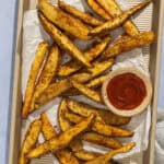 A parchment-lined baking sheet with oven baked fries and a small bowl of ketchup.
